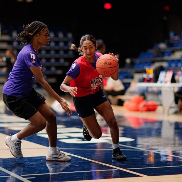 A girl wearing a red Midnight Basketball shirt dribbles the basketball while a girl wearing a purple Midnight Basketball shirt tries to block her.