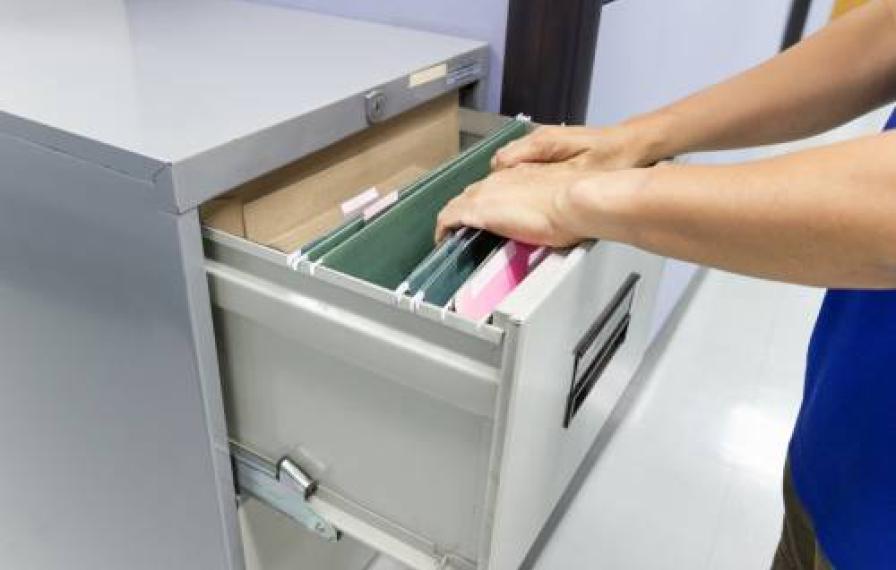 hands looking through grey file cabinet with green file folders inside.