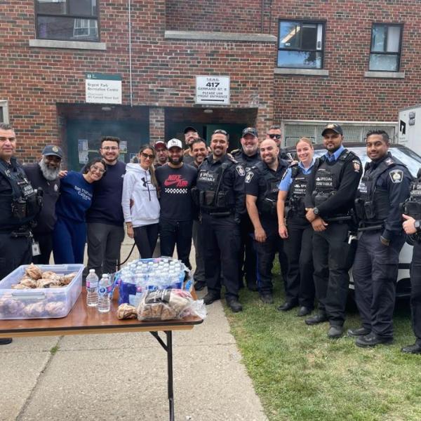 Community Safety Unit staff and other TCHC smiling for camera in front of a TCHC building with tables set up for a barbecue.