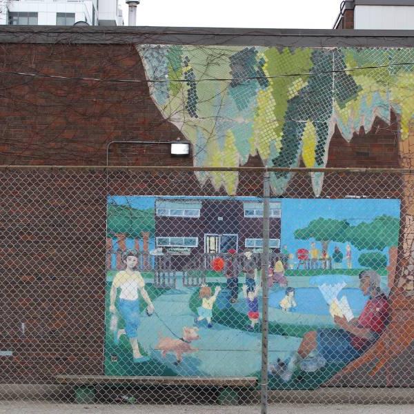 Colorful mural on a brick wall in Alexandra Park community behind a chain link fence.
