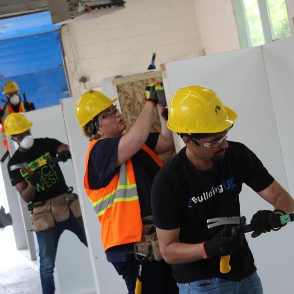 Three Building UP participants using a hammer and crowbar in a practice environment. Two more participants are in the background.