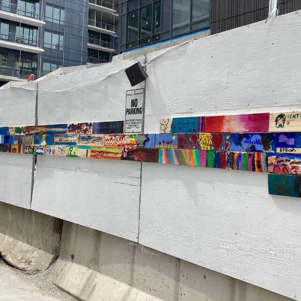 A wall of individual colourful paintings hung up on construction boards