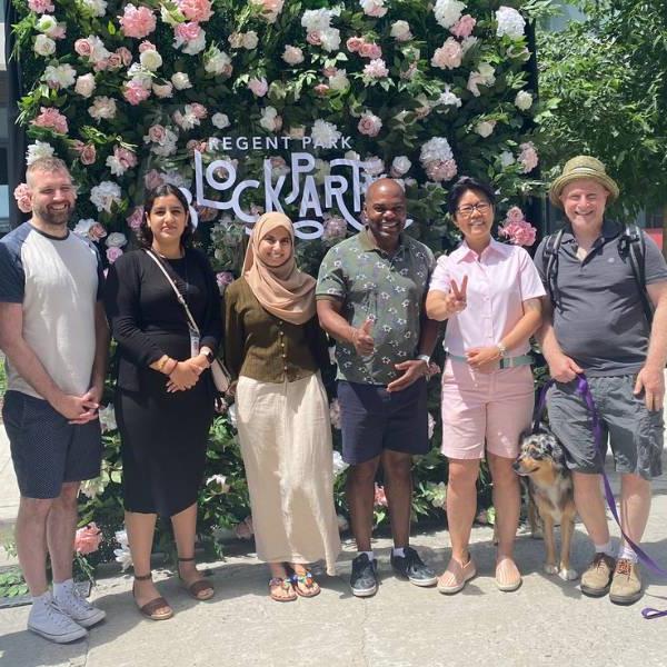 TCHC staff, Councillor Moise and MPP Wong-Tam standing in front of a sign made of flowers and greenery that says 'Regent Park Block Party'