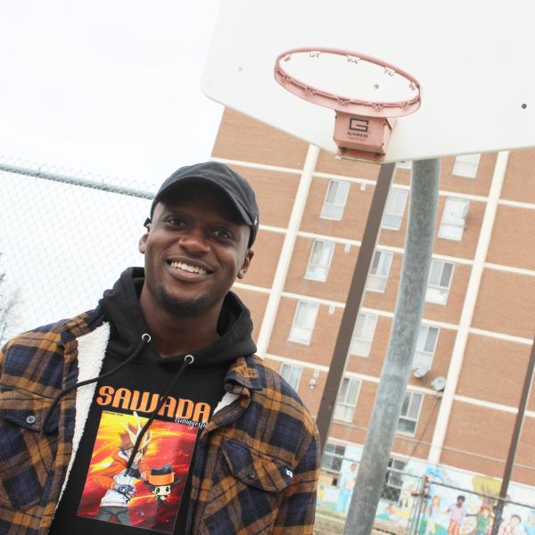 Man standing under an outdoor basketball hoop and smiling