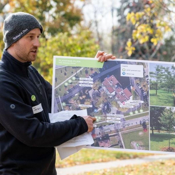 A man holding a map and pointing to different species of trees planted in a TCHC community
