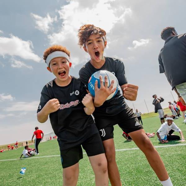 Two KickStart participants cheering to the camera by the soccer field.