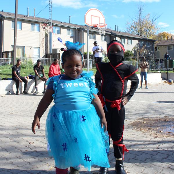 Two children posing together in halloween costumes on an outdoor basketball court