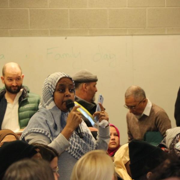 A woman wearing a blue hijab asking questions during the community meeting. 