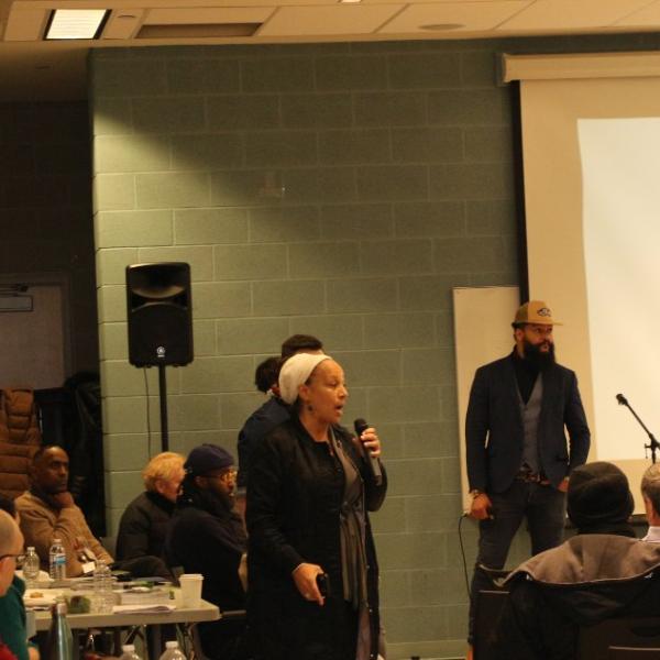 A woman wearing a black jacket speaking to community members at the meeting. 