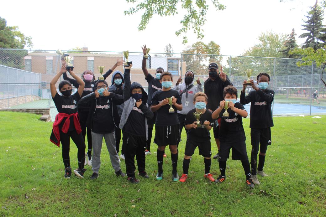 Group photo of TCHC staff and tenant youth wearing soccer outfits, cheering and holding up trophies
