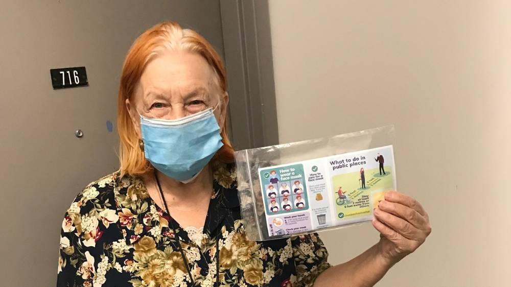 Senior Housing Unit tenant holds up information sheet on COVID-19 while wearing a free face mask that has just been delivered to their door.