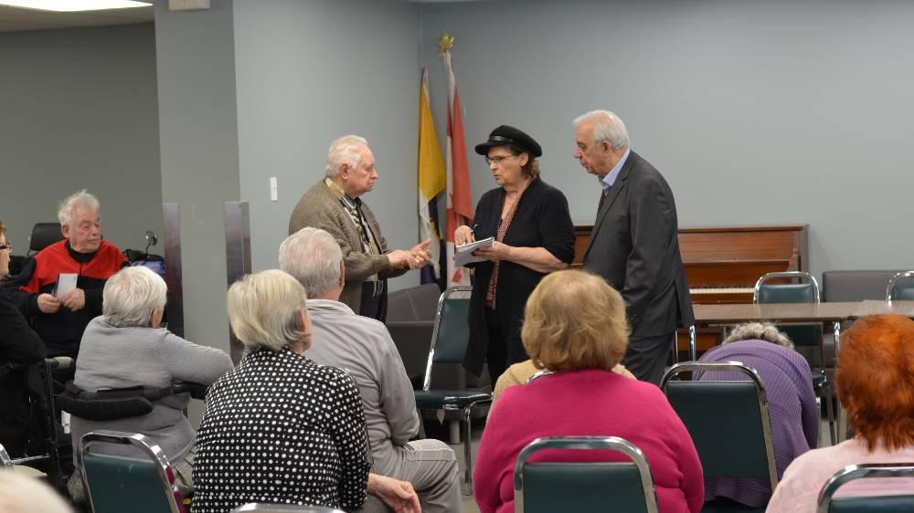 Three older people stand at the front of a room presenting to a room of seniors