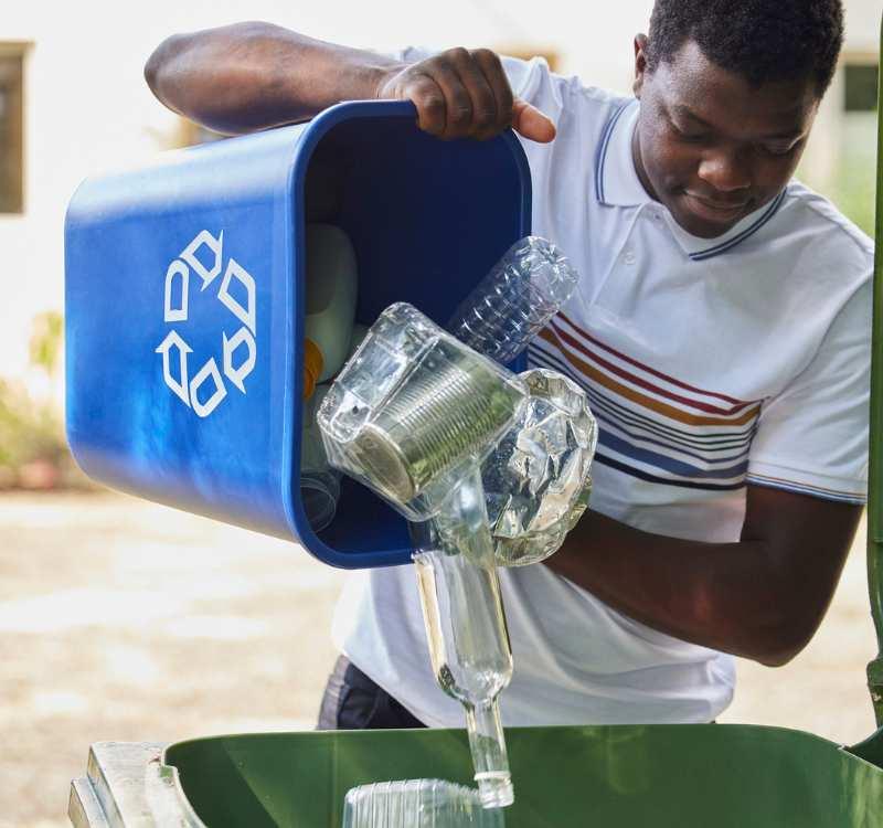 A young man recycling plastic into a green bin.