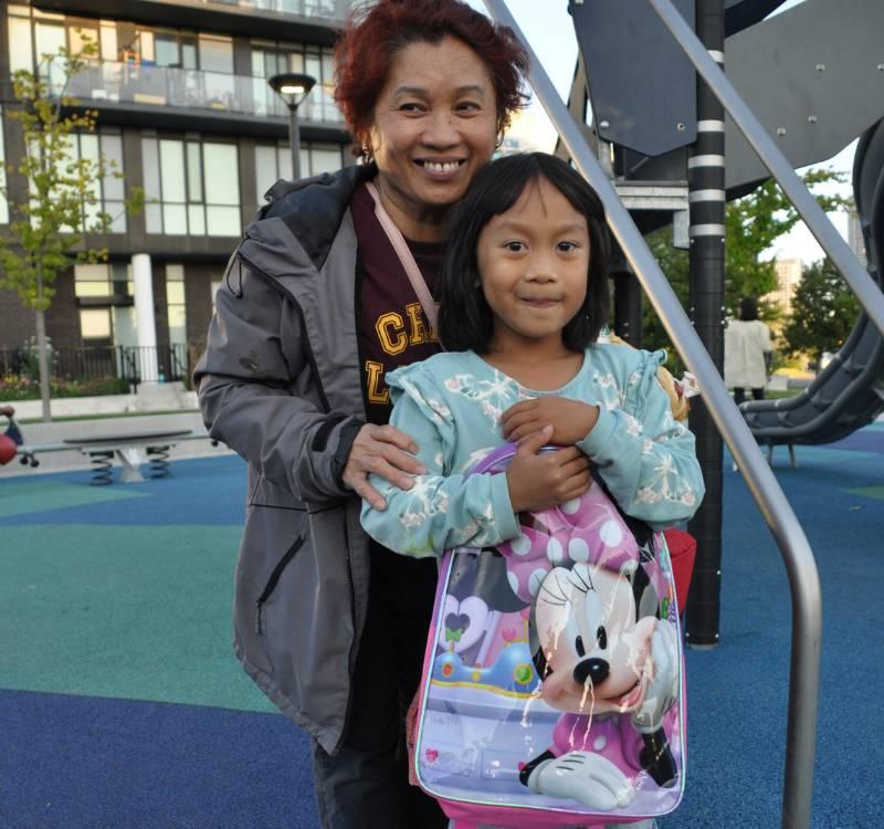 Six-year-old Mafhi and her grandmother Merlinda stand in a playground in the Allenbury Gardens community. Mafhi is holding a Minnie Mouse backpack.