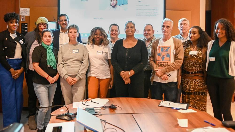 The Tenant Advisory Committee standing in a board room in front of a screen and behind a table. Tom Hunter, Interim President and CEO, and Jag Sharma, former President and CEO, are also standing with the group.