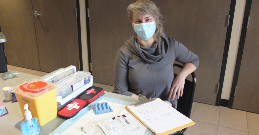 A woman wearing a mask sitting at a table with paperwork on a clipboard and first aid supplies.