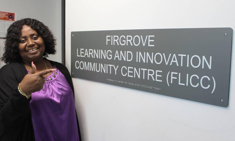 Lorraine Anderson standing beside a sign for the Firgrove Learning and Innovation Community Centre.
