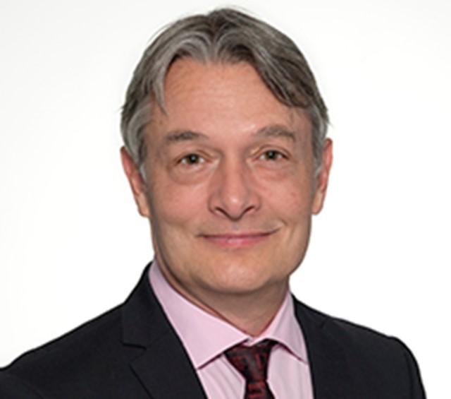 A man with grey hair wearing a suit and tie smiling at the camera.