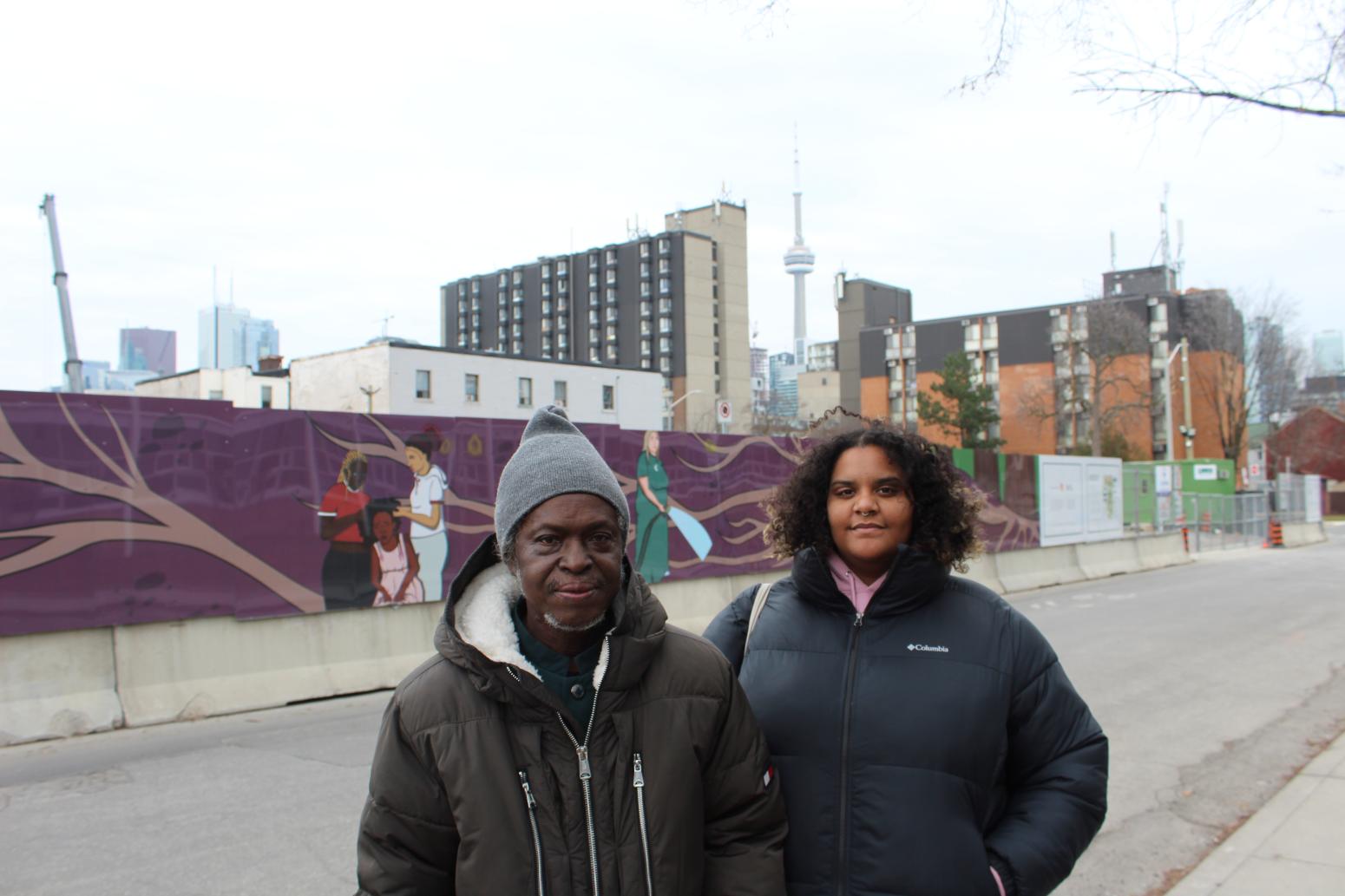 two people standing in front of a mural with CN Tower in background