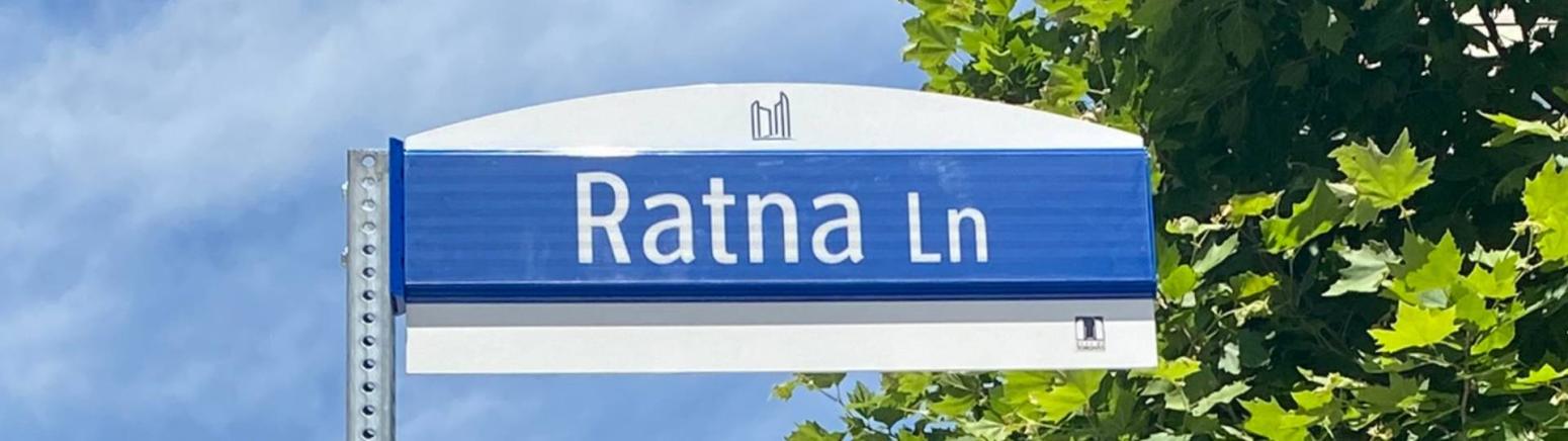 Ratna Lane street sign with the sky and trees in the background