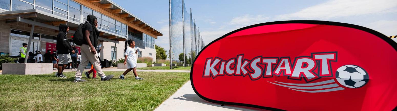 A group of participants walking past a KickStart sign onto the soccer field.