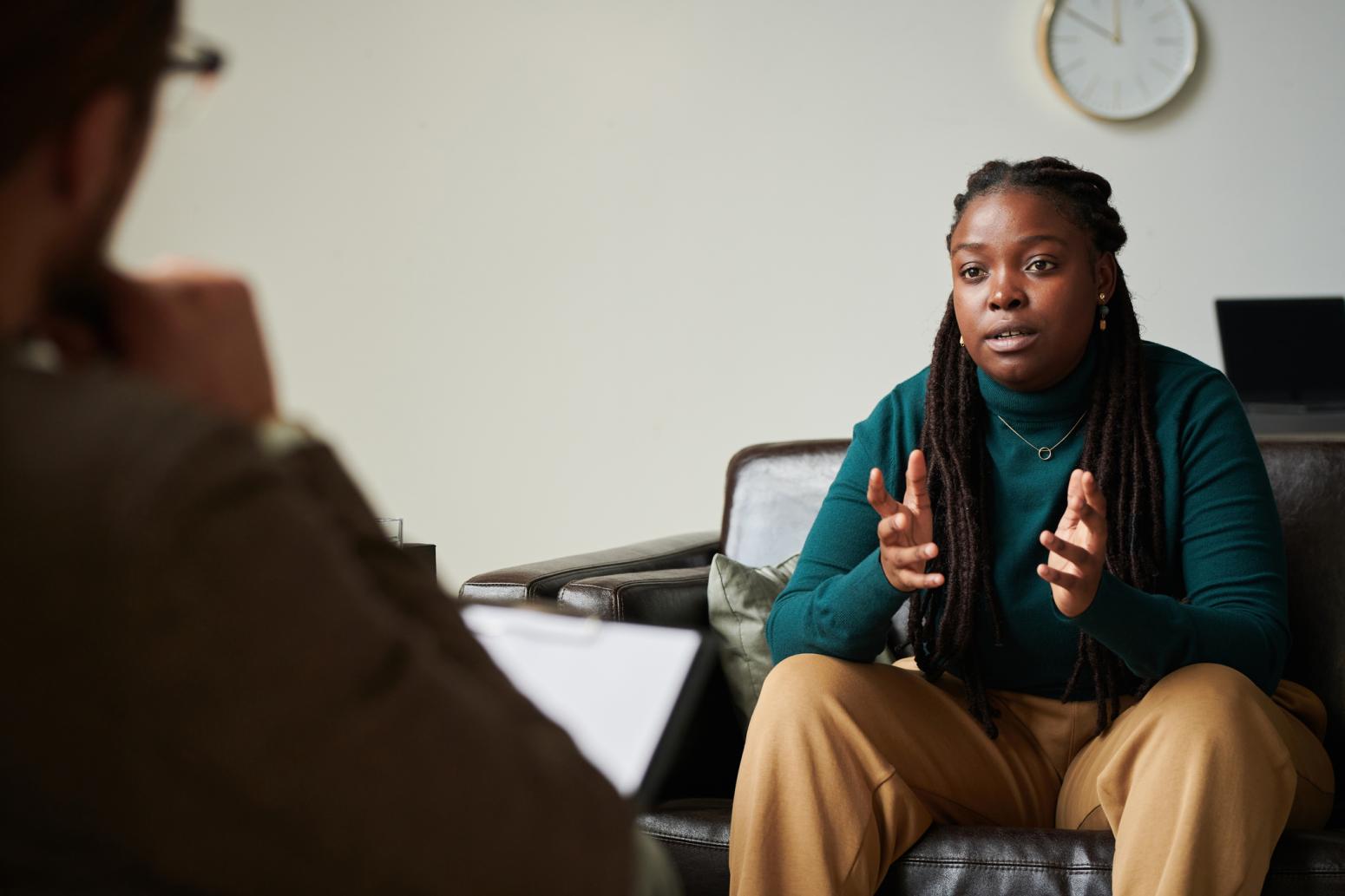 A Black woman who is wearing a green turtleneck is sitting talking to a therapist. 